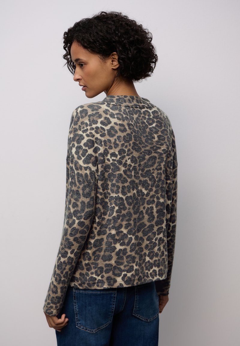 Leopardo-mönstrad stickad tröja med rund halsringning, långa ärmar och mjuk textur; har en öppen ryggdesign och avslappnad passform, i kombination med jeans.