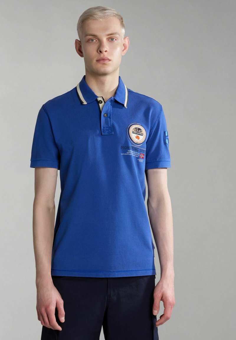 Polo shirt blu royal con colletto a contrasto, toppa con logo sul petto e testo ricamato. Maniche corte e tessuto in cotone morbido.