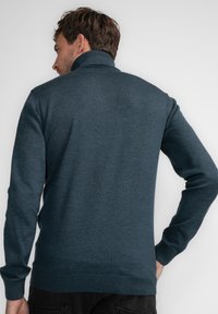 Ciemnoniebieski sweter dzianinowy z wysokim kołnierzem, ściągaczami przy mankietach i u dołu. Miękka faktura, dopasowany krój, bez widocznych wzorów ani elementów metalowych.