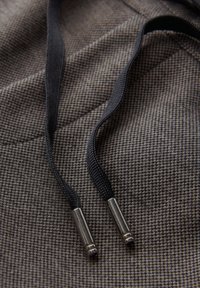 Tissu marron à motifs avec des cordons noirs dotés de pointes métalliques. La texture est tissée avec un motif de grille fine.