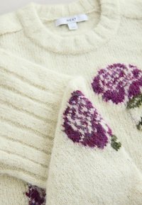 Kremowy sweter z prążkowanymi mankietami i okrągłym dekoltem, ozdobiony purpurowym haftem kwiatowym i miękkim, teksturowanym wzorem dzianiny.