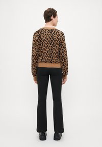 Leopard print sweater in brown and black, featuring long sleeves, ribbed cuffs, and a relaxed fit. Paired with black flared pants and chunky black shoes.