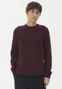 Burgunderfarbener gestrickter Pullover mit einem strukturierten Schulterbereich, der kunstvolle Muster aufweist, gerippten Bündchen und einem Rundhalsausschnitt, hergestellt aus weichem Material.