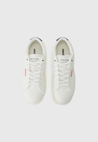 White sneakers with a smooth leather upper, lace closure, perforated detailing, and a contrasting navy accent on the heel. Brand logo visible.