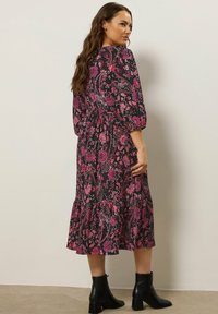 Black dress featuring a floral pattern in shades of pink, with three-quarter sleeves and a tiered skirt. Worn with black ankle boots.