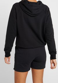 Haut à capuche noir à coupe décontractée, doté d'une capuche avec cordon de serrage et de poignets côtelés, associé à un short noir assorti. Texture de tissu douce.