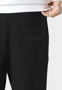 Czarne spodnie wykonane z gładkiego materiału, z subtelną tylną kieszenią i nadrukiem logo z boku. Slim fit podkreśla nowoczesny styl.