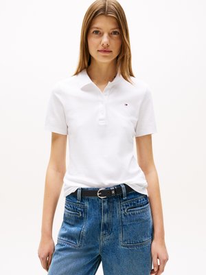 Weißes Polohemd mit drei Knöpfen, in blaue hochtaillierte Jeans aus Denim gesteckt. Schwarzer Gürtel mit silberner Schnalle. Einfaches und klassisches Design.