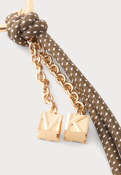 Corde marron et blanche avec un gros nœud, maillons de chaîne dorés et deux breloques carrées dorées gravées des lettres M et K.