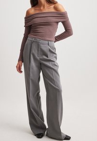 Kvinna klädd i en off-shoulder mauve långärmad topp i kombination med grå byxor med hög midja och vida ben samt svarta spetsiga skor.