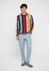 Multicolored striped sweater in red, blue, and yellow; light blue pinstriped pants; green and brown sneakers; layered with a purple shirt.