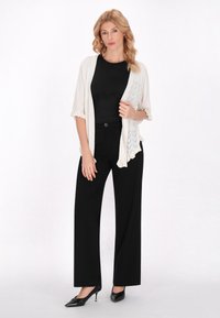 Cardigan a maglia in bianco sporco con apertura frontale e maniche corte, abbinato a un top aderente nero e pantaloni neri a gamba larga. Accenti di tacchi neri.