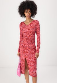 Rotes Leopardenmuster-Kleid mit langen Ärmeln, V-Ausschnitt, geraffter Taille und seitlichem Schlitz; kombiniert mit einer glänzenden pinken Handtasche.