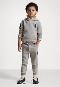 Grå hettegenser med kengurulomme og logo, kombinert med matchende joggebukser med snor, iført marineblå sneakers.