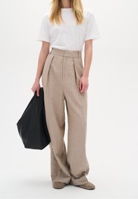 Beżowe, paskowane spodnie o szerokich nogawkach z zakładkami, zestawione z białym t-shirtem. Stylizacja obejmuje czarną skórzaną torbę oraz beżowe obuwie.