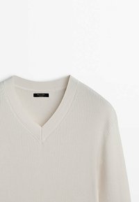 Pull crème en V avec une texture côtelée, un décolleté large et des détails cousus. Le tissu a une finition douce et lisse.