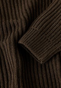 Brun, ribbad stickad tröjfabric med en texturerad mönster och veck, där tjocka, mjuka garn är synliga genom hela materialet.