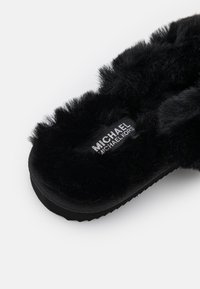 Chausson noir duveteux avec semelle épaisse et étiquette de marque Michael Kors sur la semelle intérieure, présenté sur fond blanc.