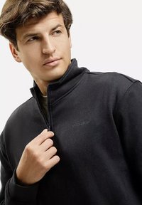 Czarny polarowy golf z wysokim kołnierzem i ćwierć zamkiem. Posiada wyszywane detale oraz subtelne logo na klatce piersiowej. Gładka tekstura.