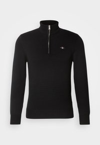 Jersey negro de punto con mangas largas, puños y bajo acanalados, cuello con cremallera hasta la mitad y un pequeño logo bordado en el pecho izquierdo.