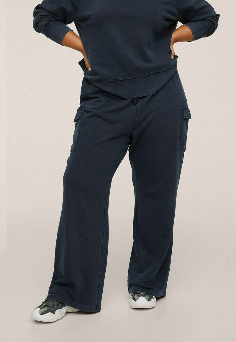 Pantalons cargo bleu marine à jambes larges, en tissu doux, avec deux poches latérales et une taille à cordon. Associés à des baskets blanches texturées.