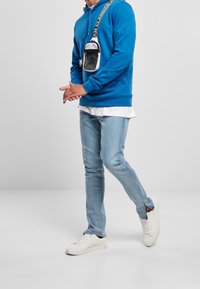 Modrá mikina s kapucí, světle modré džíny a bílé tenisky. Obsahuje malou černobílou crossbody tašku s mřížkovým detailem.