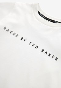 Tricou alb din bumbac cu un logo imprimat negru care spune "BAKER BY TED BAKER" centrat pe piept. Textură netedă, guler rotund.