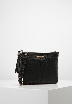 Czarna teksturowana torebka na ramię z złotym łańcuszkiem, ozdobą z chwostem oraz małą złotą plakietką z logo na przodzie, umieszczona na białej powierzchni.