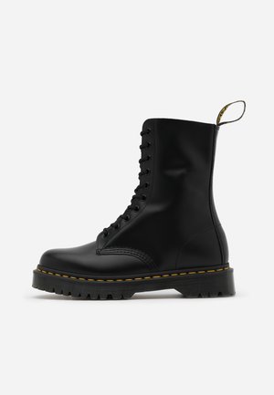 Black leather lace-up ankle boot with a chunky sole, yellow stitching, and a pull tab at the back for easy wearing.