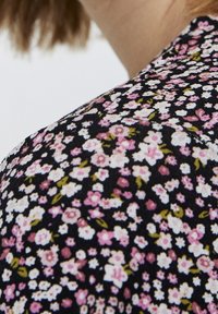 Tissu noir avec un petit motif floral en rose et blanc, accompagné de feuilles vertes. La texture semble douce et légère.