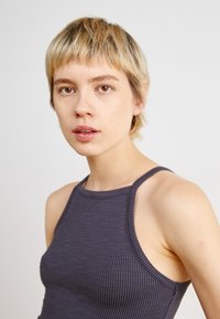 Grå ribbad tanktopp med hög halsringning och tunna axelband. Tyget verkar slätt med en subtil textur.