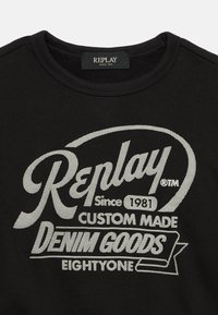Felpa nera a collo rotondo con testo bianco: "Replay Since 1981 Custom Made Denim Goods Eightyone" e etichetta del marchio all'interno del colletto.