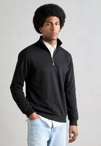 Black pullover sweatshirt with a quarter-zip collar, ribbed cuffs, and a smooth texture, worn over a white collared shirt.
