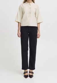 Beige randig topp med utsvängda ärmar och en krusidullkrage, knäppning fram. Kombinerad med svarta raka byxor och mörka klackar.