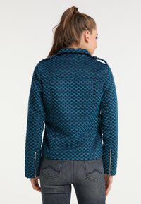 Niebieska i czarna kurtka o fakturowanej strukturze z dopasowanym fasonem, z kołnierzem, zamkami na rękawach oraz widocznymi detalami szycia.