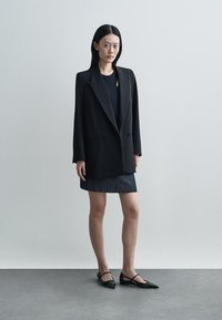 Μαύρο oversized μπλέιζερ με κεντρωμένα καπέλα, συνδυασμένο με εφαρμοστό μαύρο τοπ και σκούρα τζιν φούστα. Μαύρες άκρες με σταυρωτές λωρίδες.