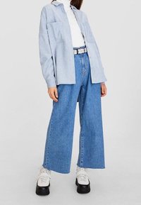 Jasnoniebieska, oversize'owa koszula z dwiema kieszeniami z przodu, biała golf, dżinsy z szerokimi nogawkami oraz masywne czarno-białe sneakersy.