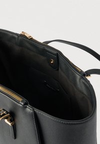 Čierna kožená kabelka so zlatým zipsom a prackou, otvorený vrch odhaľuje priestranný čierny textilný interiér s malým vnútorným vreckom.