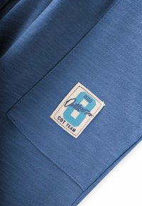 Blaues Baumwollgewebe mit einer glatten Textur. Enthält ein rechteckiges Etikett mit einer großen Zahl "6" in türkis und schwarzem Text.