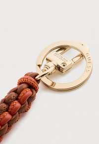 Portachiavi intrecciato realizzato in pelle marrone e arancione con un gancio metallico dorato che presenta il logo "GUESS" e un design circolare.