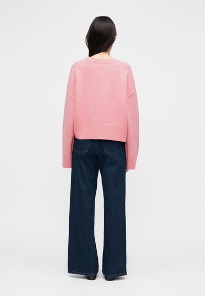 Κοντή ροζ μπλούζα με ριμπ τελείωμα, χαλαρή εφαρμογή, φορεμένη με ψηλόμεσα, φαρδιά παντελόνια από σκουρόχρωμο denim, όψη από πίσω.
