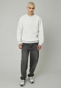 Sweatshirt gris clair avec un col rond et des manches à poignets, assorti à un jean gris foncé à coupe décontractée et des baskets blanches et argentées.