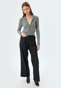 Maglione grigio a zip in maglia con maniche lunghe, abbinato a pantaloni neri a righe verticali a vita alta e stivaletti neri con punta.
