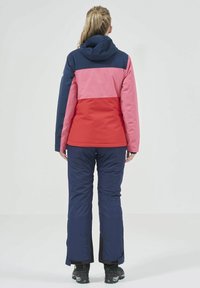 Giacca a blocchi di colore in blu navy, rosa e rosso con cappuccio; abbinata a pantaloni blu navy. Presenta una texture liscia e una vestibilità comoda.