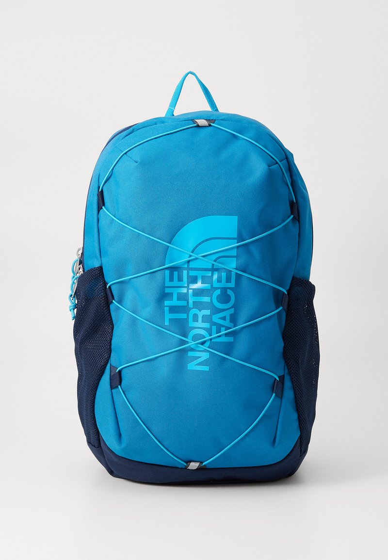 Mochila azul com um tecido texturizado, apresentando um logótipo, cordas elásticas de bungee na frente e bolsos laterais em malha azul-marinho.