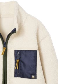 Fleece jacket in cream with a navy pocket. Features a zip closure, high collar, and contrasting green zipper. Includes a brand logo patch.