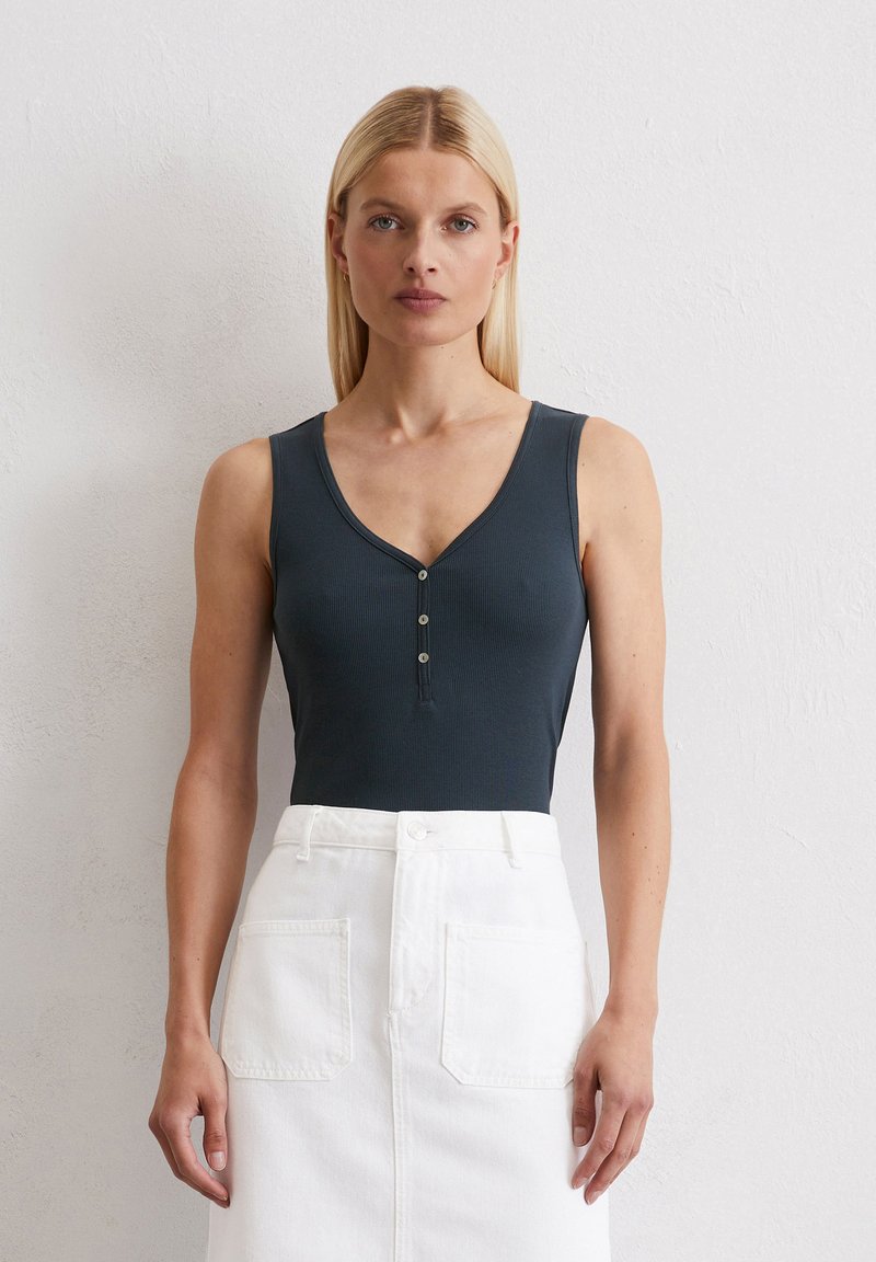 Donkergrijs geribbeld body met een diepe V-halslijn en drie knopen aan de voorkant, gecombineerd met een witte denim rok met achterzakken.