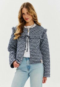 Niepikowany granatowo-biały płaszcz w krateczkę z falbanami, wiązaniami przy kołnierzu oraz długimi rękawami, zestawiony z jasnoniebieskimi dżinsami.