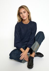 Marinblå striktrøje med struktureret mønster, rund halsudskæring og sænkede skuldre, parret med brede denimjeans og sorte loafers.
