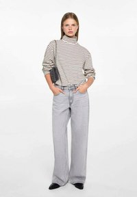 Beige with dark stripes turtleneck sweater, paired with light grey wide-leg jeans and black pointed-toe shoes. Small black handbag.